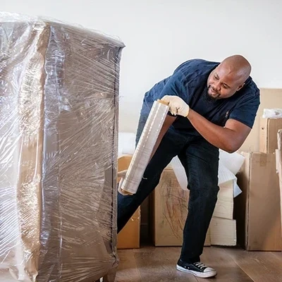 African man neatly wraps a large box with cellophane in preparation for self storage