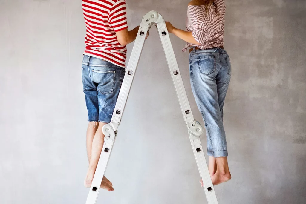 A young couple stood on either side of a ladder while renovating their home