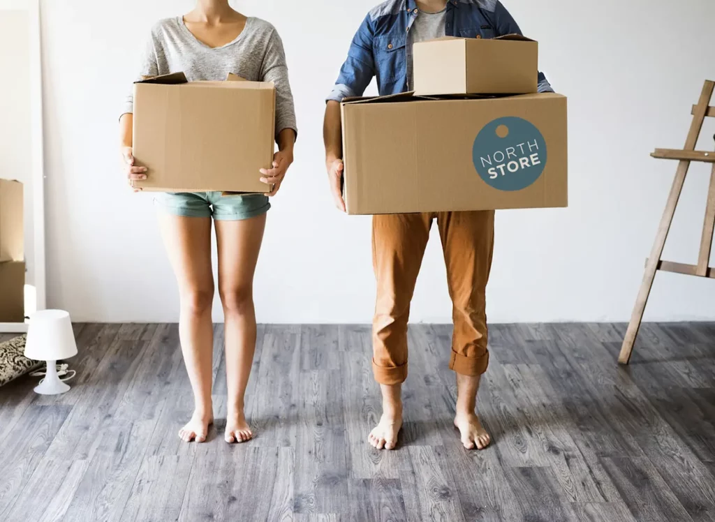 Happy young couple holding boxes for self storage in a starter apartment, moving or renovating the sapce.